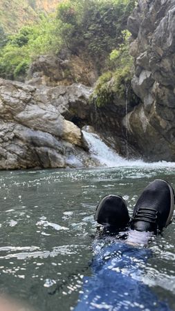 Person's water shoes in pond below waterfall