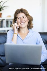 Businesswoman sitting on sofa at home using a laptop and chatting on phone 5r9LXl