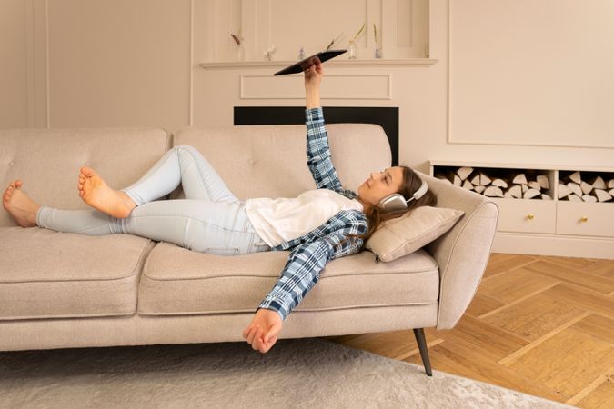 Relaxed teen girl lying on sofa taking tablet selfie.