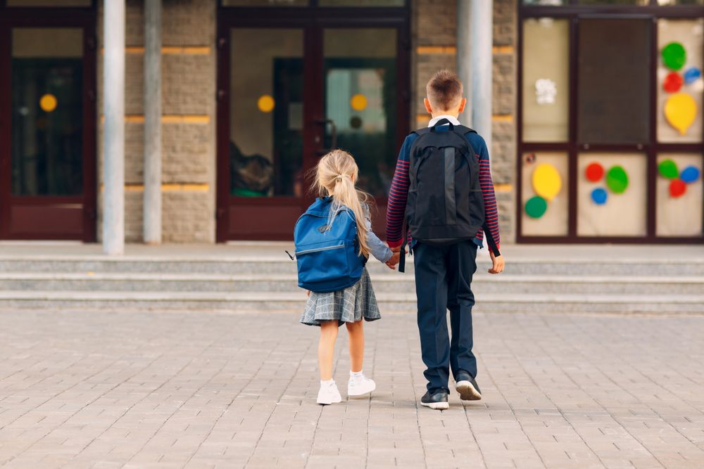 Back view of brother and sister holding hands walking to school