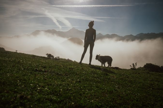 Adult tourist with dog against foggy valley under clear sky in summer