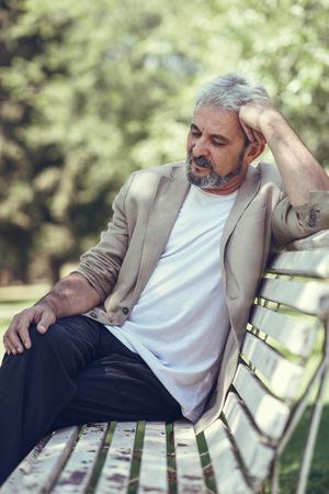 Portrait of a grey haired man, lost in thought on bench in a park