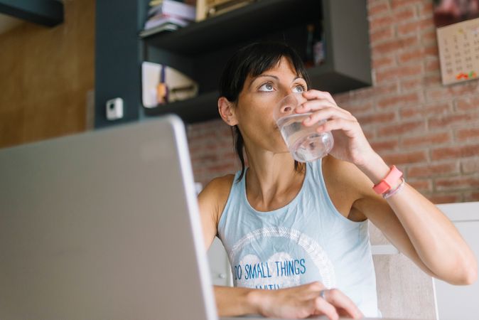 Woman sipping water while sitting at laptop