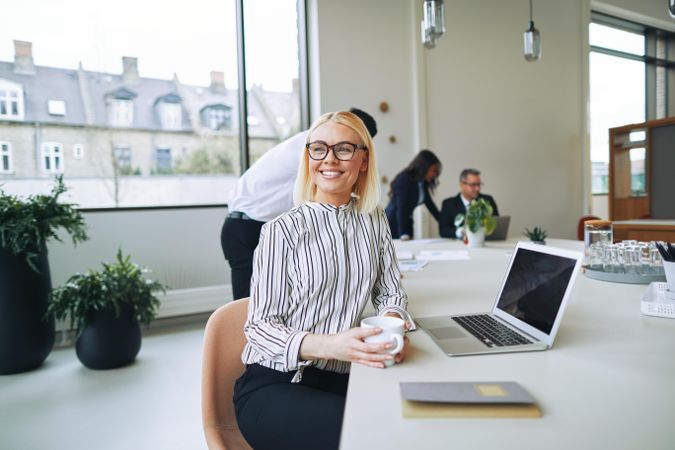 Woman looking up from her laptop and smiling in a bright office with coffee