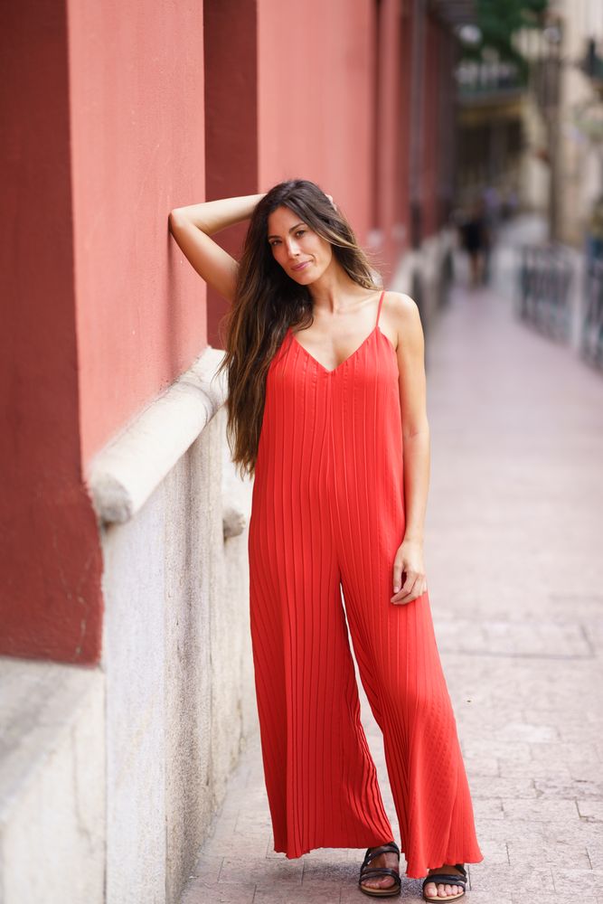 An Elegant Woman Dressed in a Stunning Red Jumpsuit Posing Gracefully Against a City Wall