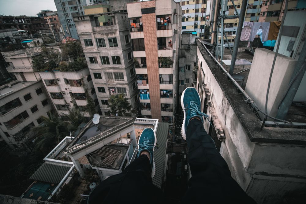Person in dark pants and blue sneakers sitting on top of building
