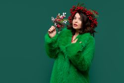 Elegant woman in green coat and berry wreath enjoys a festive bouquet.