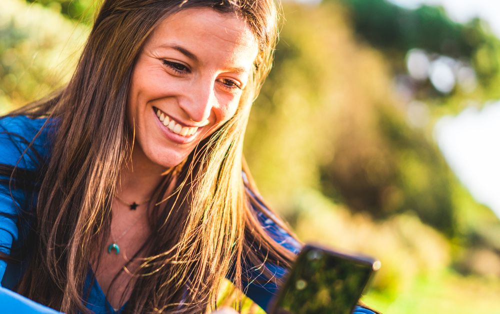 portrait of young woman using smartphone sitting on grass in park