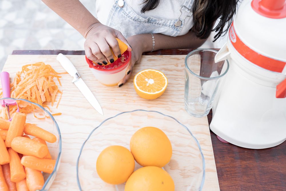 A young Hispanic woman is squeezing an orange to make orange and carrot juice outdoors