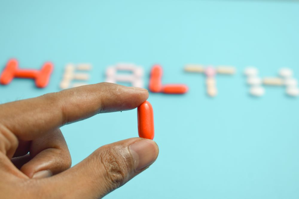 Person holding pill in front of "HEALTH" spelled on blue background