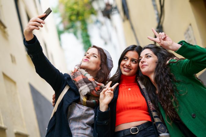 Three happy female friends dressed in fall clothes taking selfie