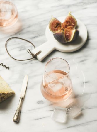 Rose wine in glass on marble table with quartered fig and knife