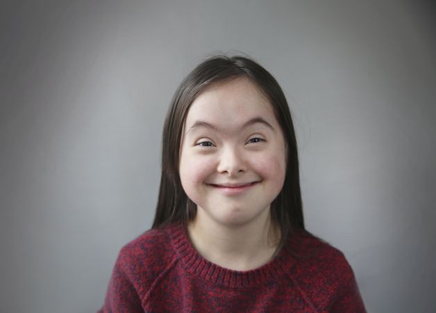 Adorable girl with Down syndrome smiling and looking at camera in studio setting