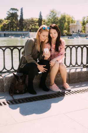Multiethnic friends using smartphone on embankment