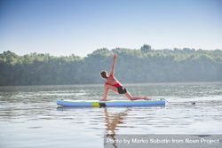 Woman stretching hips on paddleboard on lake in the morning 5alVQ0