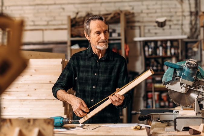 Bearded carpenter measuring wood in his studio