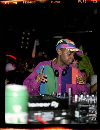 Young male DJ in colorful retro 90s garb performs on mixer and turntables