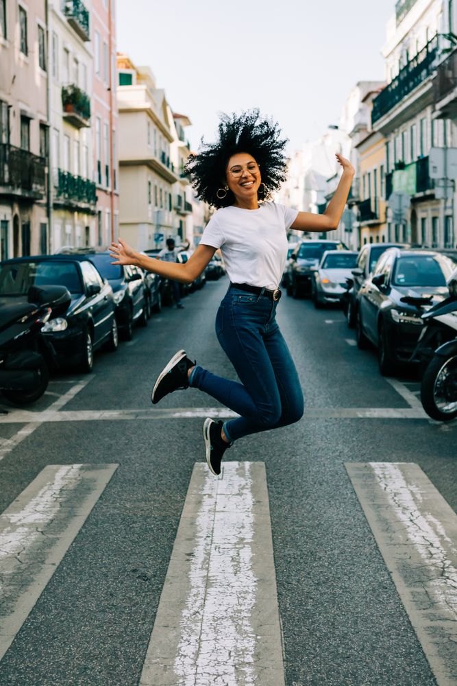 Happy Black female jumping on crosswalk