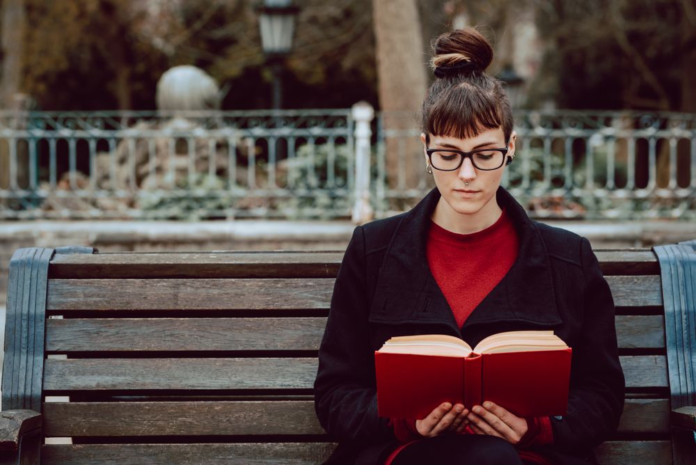 Young woman reading book on bench in park
