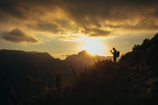 Silhouette of man taking pictures of mountain valley with his smartphone at sunset
