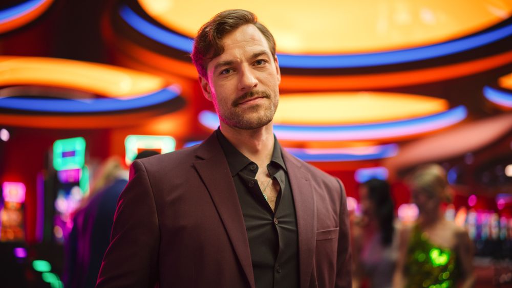 Young Man with a Moustache Standing in the Glamorous Colorful Atmosphere of a Casino