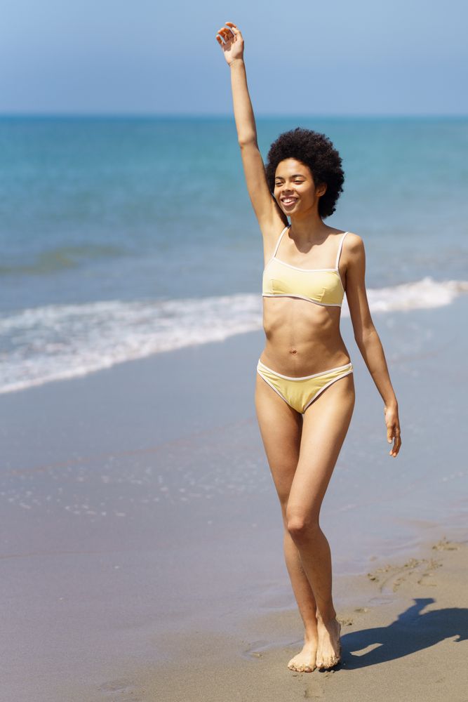 Woman walking next to the sea with arm up in yellow bikini