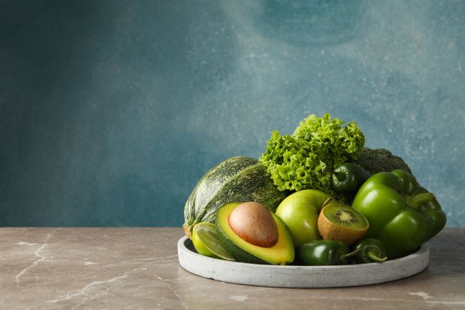 Tray with green fruits and vegetables on gray table