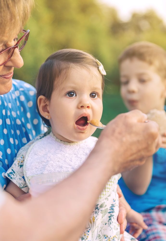 Grandparents feeding baby girl sitting on a bench