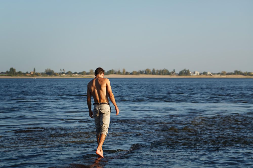 Male walking on shallow rocks in a lake