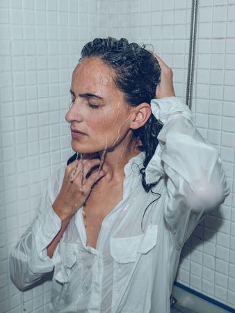 Exhausted woman in wet clothes under pouring water in bathroom