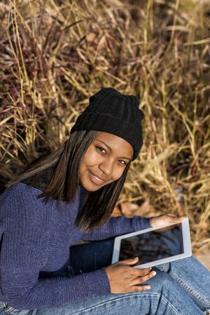 Female in hat and sweater sitting in grass with tablet