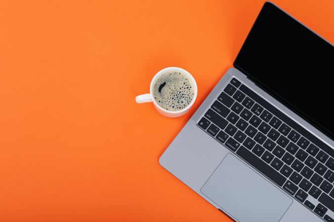 Laptop on orange desk with mug of coffee or tea and ear buds with copy space