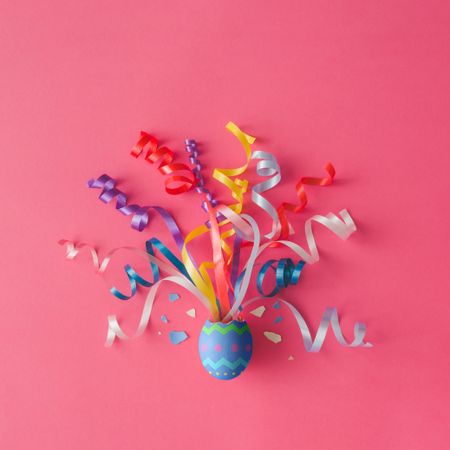 Painted Easter egg with party streamers on pink background
