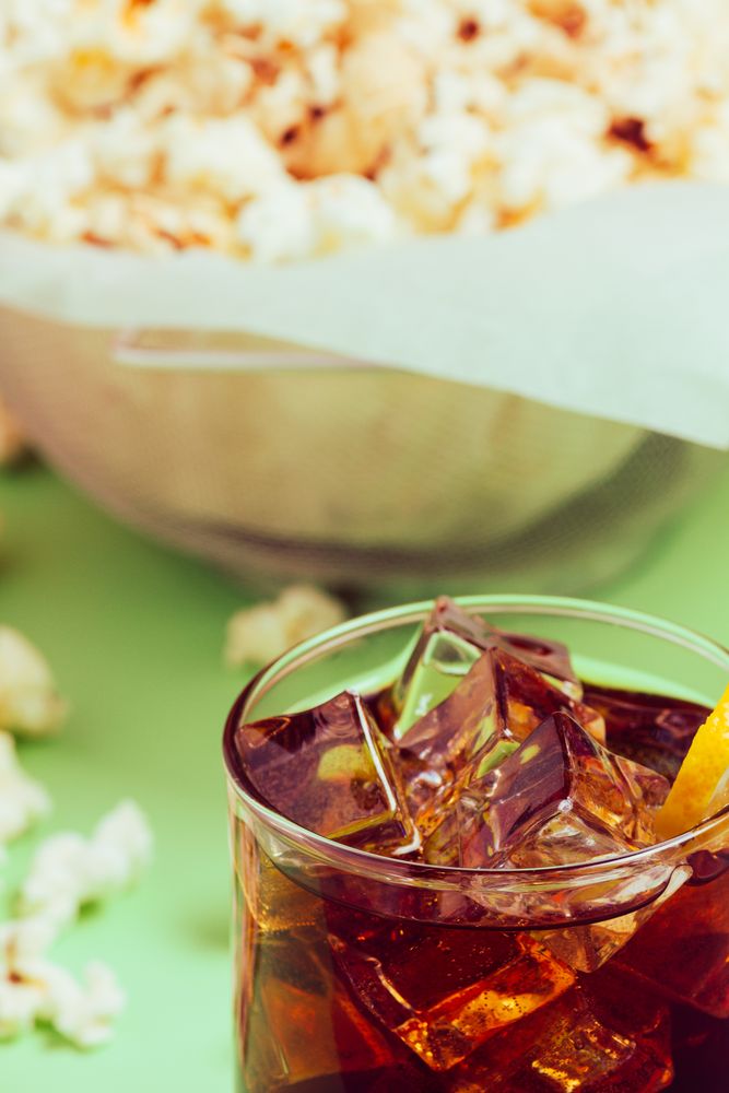 Popcorn in bowl near drink in glass with ice and lemon
