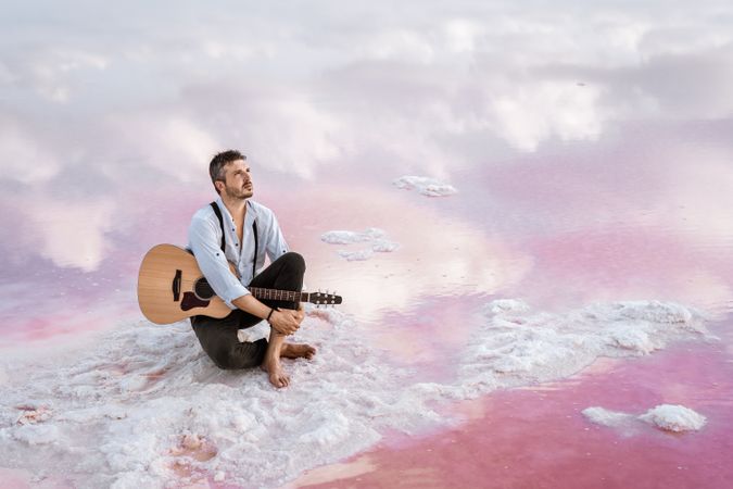 Musician with guitar on pink sandy water