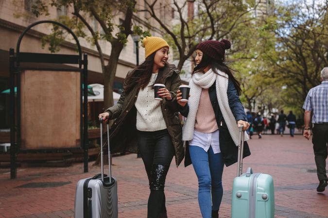 Two young women smiling at each other walking with suitcases