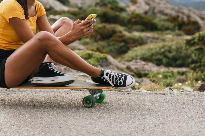 Anonymous woman using mobile phone while sitting on longboard