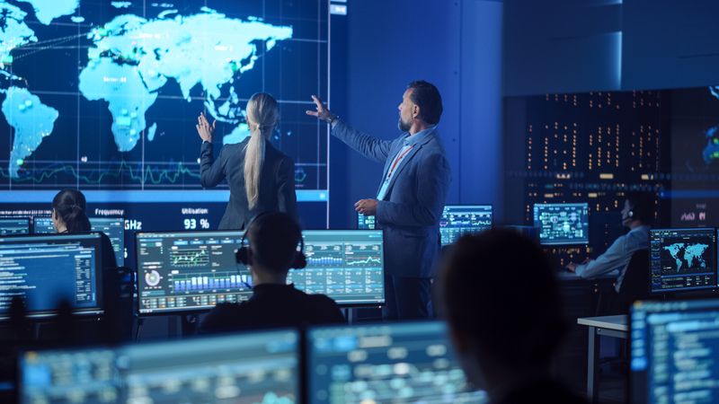 Executives Discuss Global Strategy in High-tech Control Room. Analysts Monitor Data on Multiple Screens. Large World Map Display Dominates, Showcasing International Operations and Real-time Information Flow.
