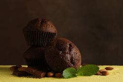 Composition with tasty muffins, chocolate and nuts on yellow table