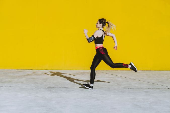 Woman with earphones running near wall