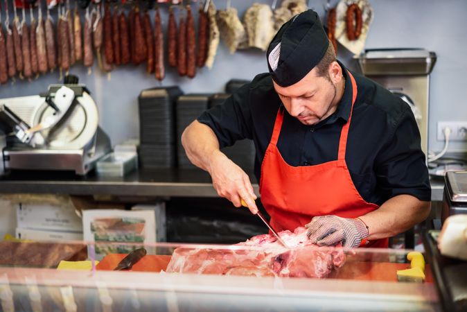 Man cutting ham behind counter in butcher shop