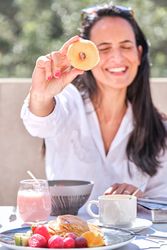 Laughing woman showing donut sitting at table with served breakf