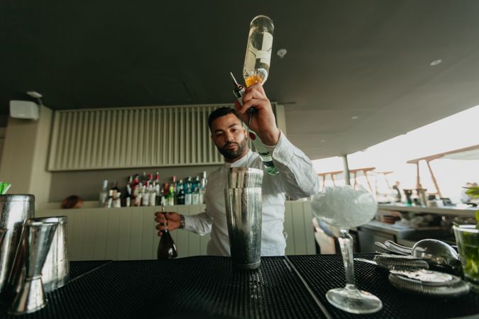 Barman pouring cocktail and alcoholic drinks to shaker in a bar.