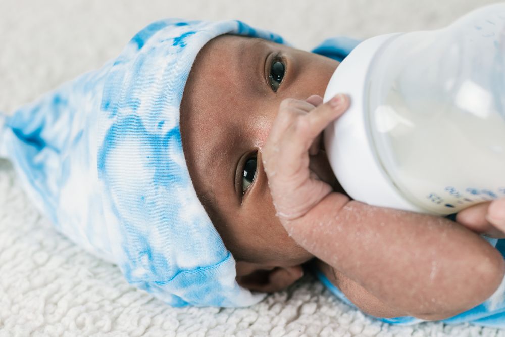 Anonymous mother feeding newborn baby wrapped on soft blanket