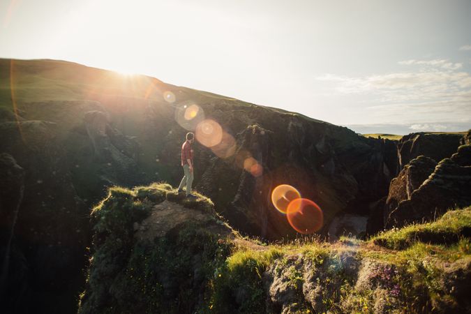 Man relaxing on edge of cliff with sun flare
