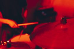Anonymous man with drumsticks playing on drums in redness