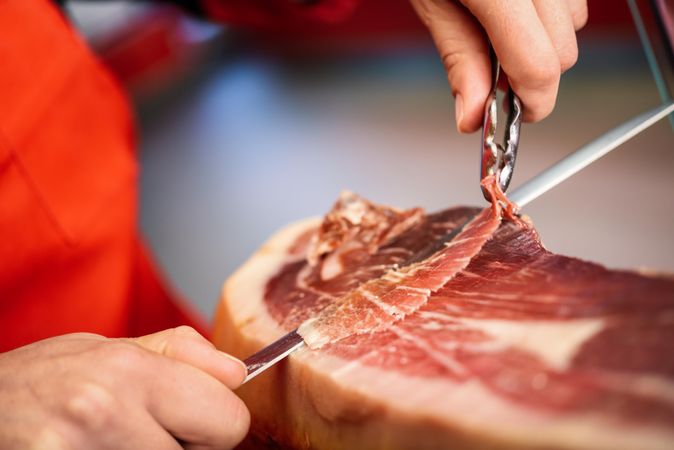 Close up of female hands in butcher shop slicing ham
