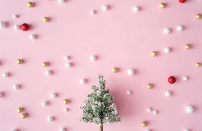 Different shades of pink and light-colored baubles on a pink background with snowy tree