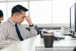 Stressed Asian male employee sitting at desk in the office 4BGvXb