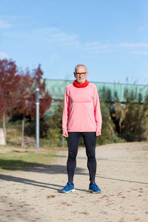 Grey haired man in red shirt and glasses standing in park in exercise gear
